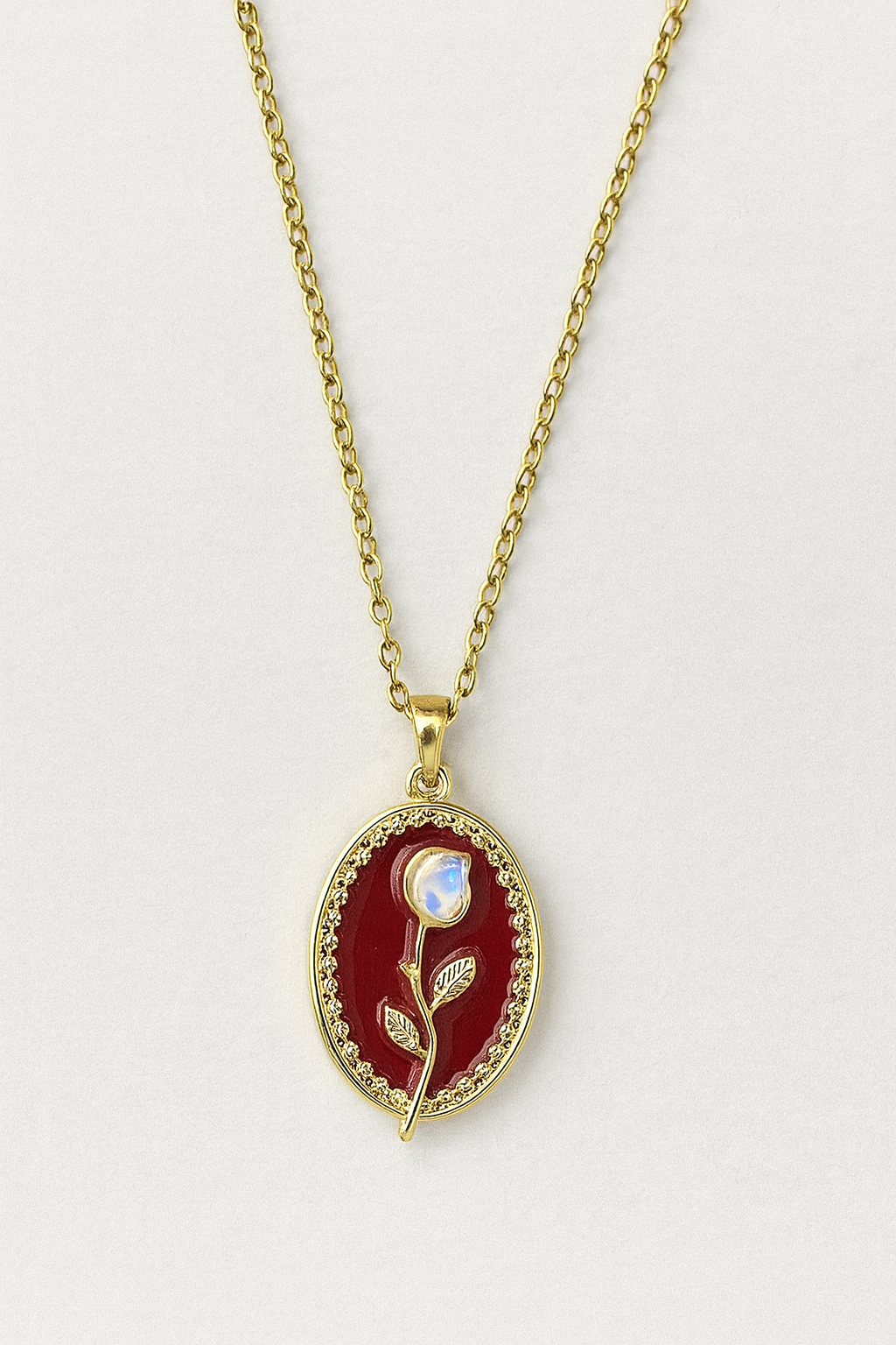 Gold necklace with an oval red pendant featuring a white rose.